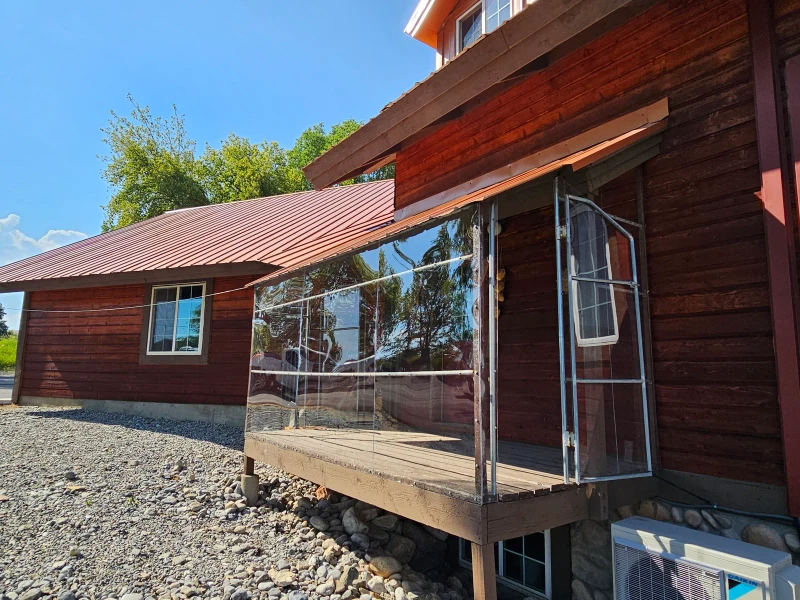 Finished clear-panel deck enclosure on a log home with a red metal roof in Cache Valley