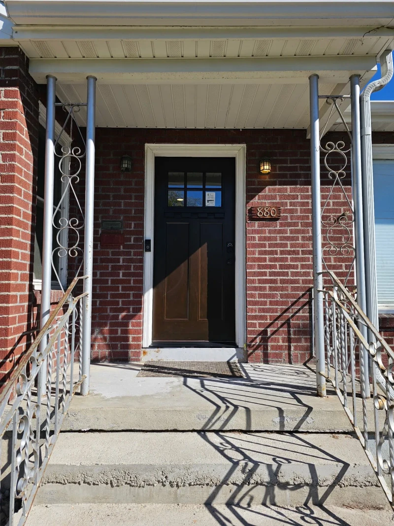 New dark craftsman-style front door with a six-pane window in the brick entry under the covered porch