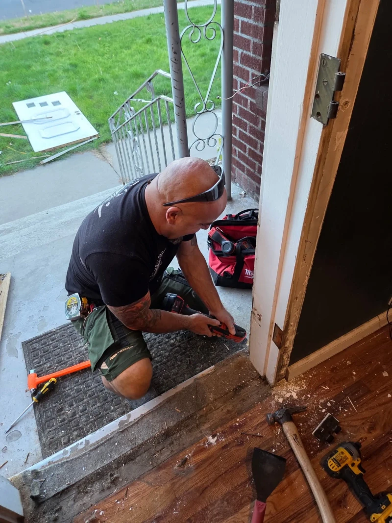 S&C Handyman technician cutting out the old threshold with an oscillating tool, the old door lying on the lawn behind him
