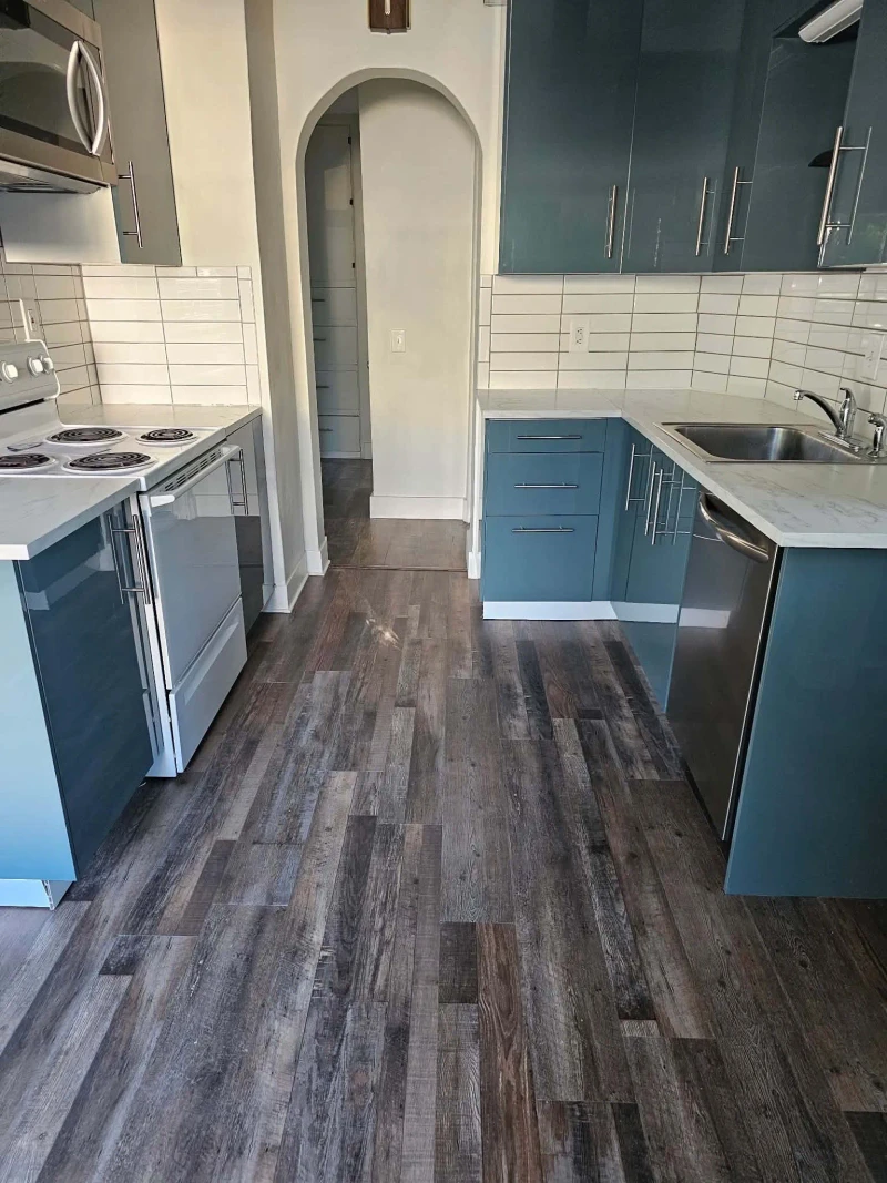 Finished kitchen with rustic wood-look luxury vinyl plank flooring under blue gloss cabinets, white subway tile and an arched doorway