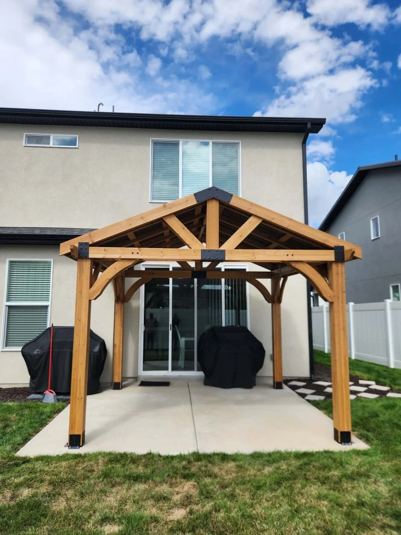 Completed cedar timber-frame pavilion seen straight on from the lawn, framing the patio doors of the two-story home