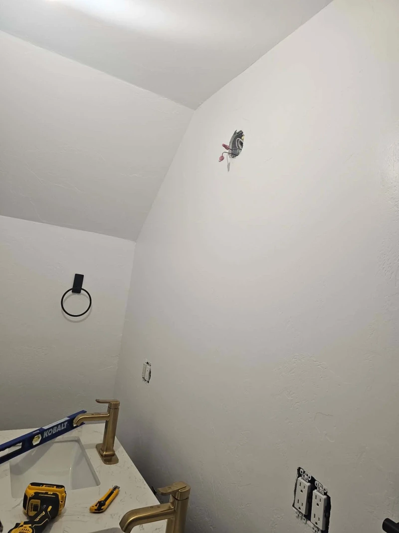 Bare junction box wired above the vanity and ready for the new light fixture, with the gold faucets already installed below